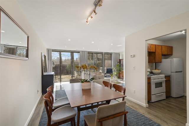 dining space featuring baseboards, wood finished floors, rail lighting, floor to ceiling windows, and recessed lighting