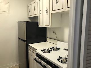 kitchen featuring baseboards, freestanding refrigerator, white gas range, light countertops, and white cabinetry