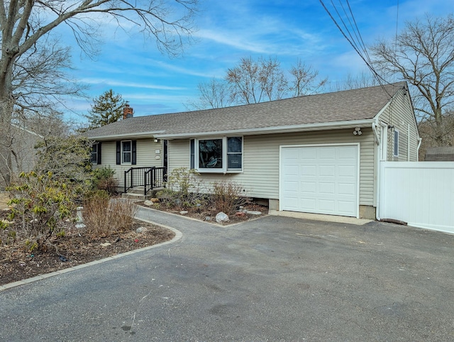 ranch-style home with a garage, fence, driveway, roof with shingles, and a chimney