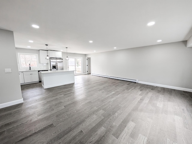 unfurnished living room with recessed lighting, a baseboard heating unit, a sink, baseboards, and dark wood finished floors