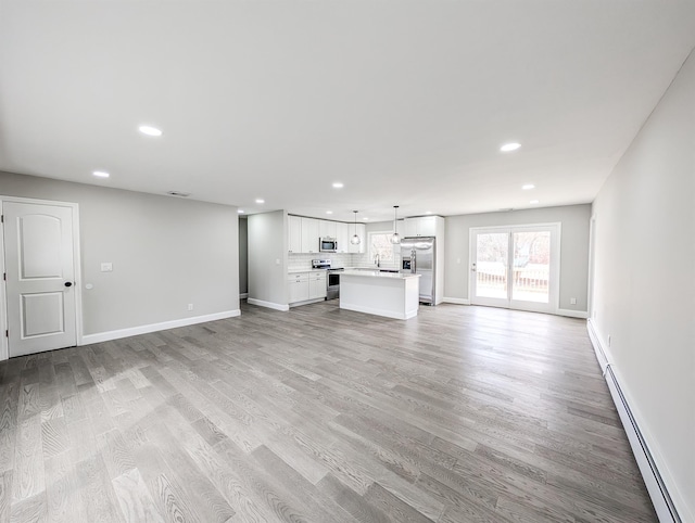 unfurnished living room with light wood-style floors, a baseboard radiator, baseboards, and recessed lighting