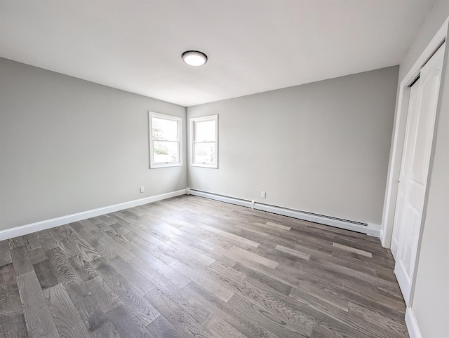 unfurnished bedroom with a baseboard radiator, a closet, baseboards, and wood finished floors