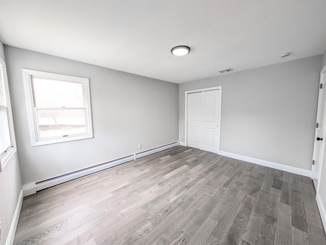 unfurnished room featuring a baseboard heating unit, wood finished floors, visible vents, and baseboards