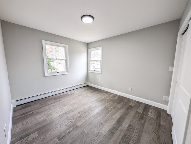 spare room with a baseboard heating unit, dark wood finished floors, and baseboards