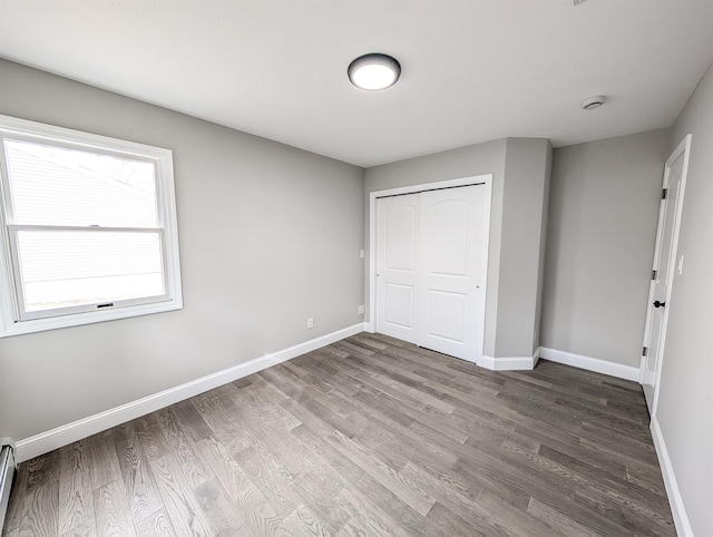 unfurnished bedroom with a baseboard radiator, baseboards, and wood finished floors