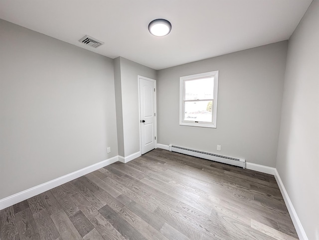 spare room with baseboards, visible vents, baseboard heating, and wood finished floors