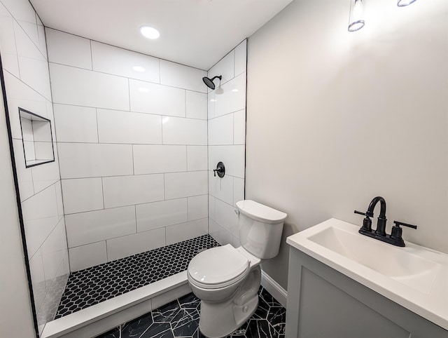 full bath featuring vanity, a tile shower, toilet, and baseboards