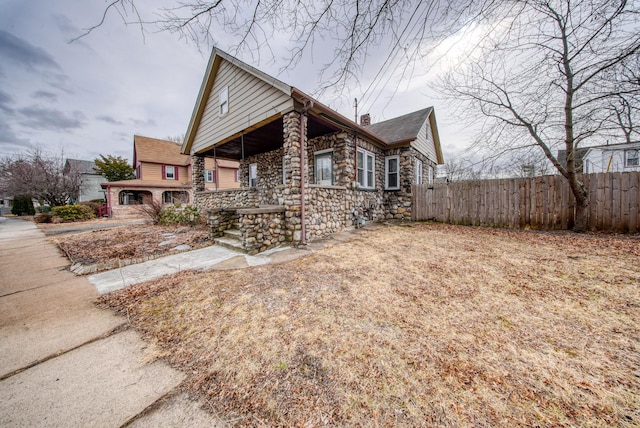 view of front of property with stone siding, a chimney, fence, and covered porch