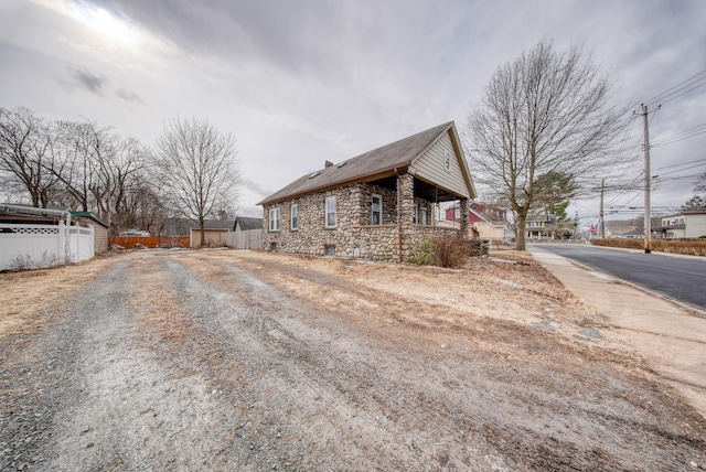 view of home's exterior featuring driveway, stone siding, and fence