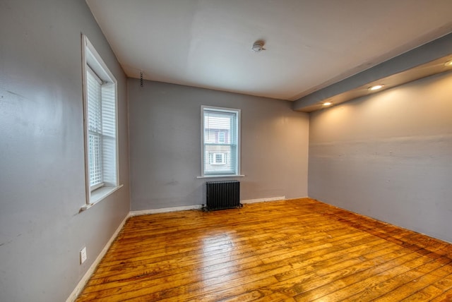 spare room featuring radiator heating unit, hardwood / wood-style flooring, and baseboards