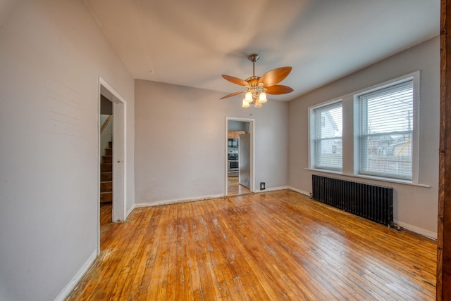 spare room featuring light wood finished floors, radiator, stairway, a ceiling fan, and baseboards