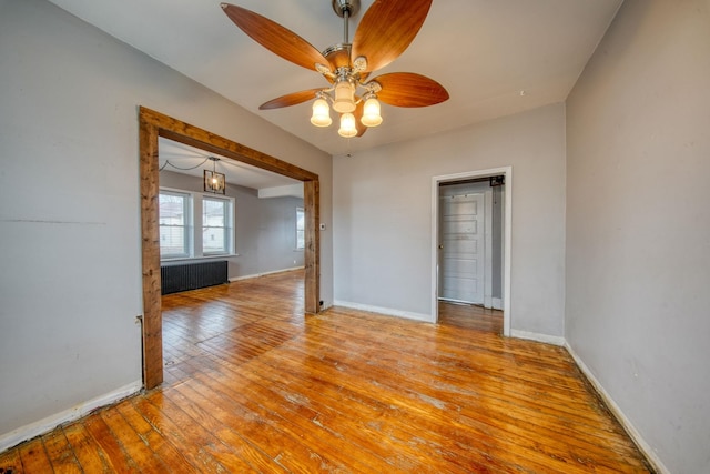 unfurnished room featuring baseboards, a ceiling fan, hardwood / wood-style flooring, and radiator