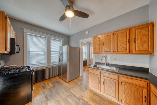 kitchen featuring stainless steel refrigerator with ice dispenser, gas range oven, light wood-style flooring, a sink, and black microwave