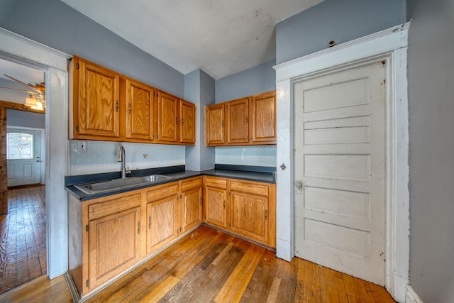 kitchen with decorative backsplash, brown cabinetry, dark countertops, hardwood / wood-style flooring, and a sink