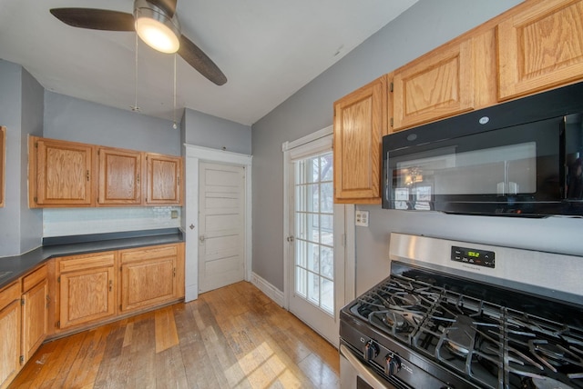 kitchen featuring stainless steel gas range oven, dark countertops, ceiling fan, light wood-style flooring, and black microwave