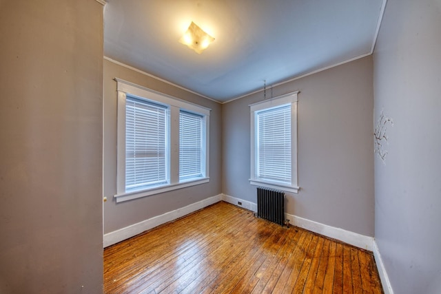 spare room with baseboards, crown molding, hardwood / wood-style floors, and radiator heating unit