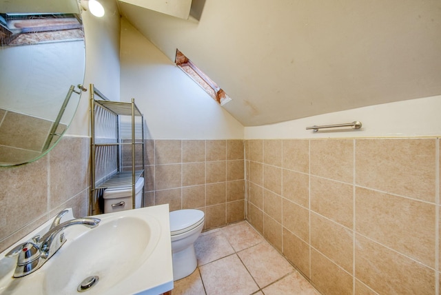 bathroom with vaulted ceiling with skylight, toilet, a wainscoted wall, tile patterned flooring, and tile walls