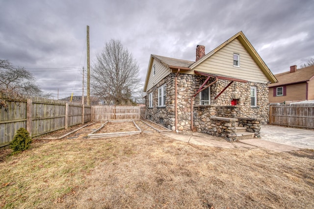 rear view of house with a fenced backyard, stone siding, a vegetable garden, a chimney, and a patio area