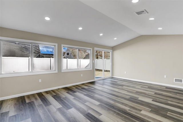 empty room with vaulted ceiling, wood finished floors, visible vents, and baseboards