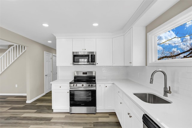 kitchen with stainless steel appliances, light countertops, white cabinetry, a sink, and light wood-type flooring