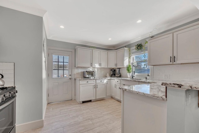 kitchen featuring light stone counters, range with gas cooktop, crown molding, tasteful backsplash, and a sink