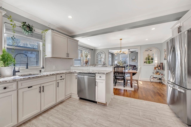 kitchen featuring light stone counters, crown molding, appliances with stainless steel finishes, a sink, and a peninsula