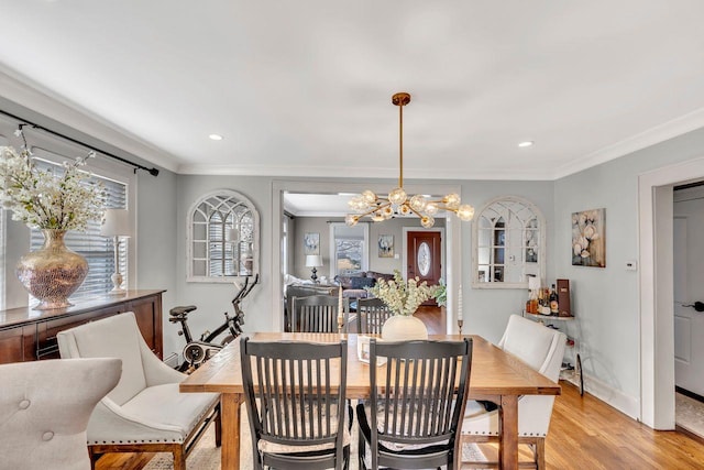 dining area with light wood-style floors, a wealth of natural light, ornamental molding, and an inviting chandelier