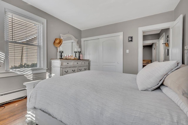 bedroom with a closet, baseboard heating, and wood finished floors