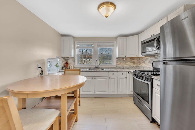 kitchen with tasteful backsplash, appliances with stainless steel finishes, white cabinets, a sink, and light stone countertops