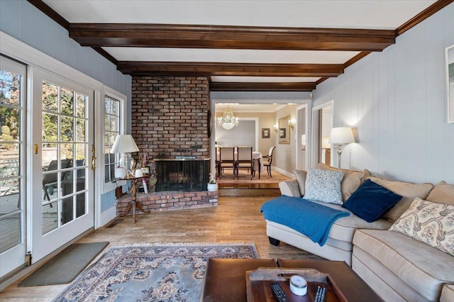 living room featuring crown molding, beamed ceiling, a fireplace, wood finished floors, and a notable chandelier