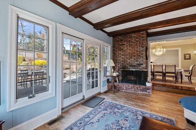 living room with visible vents, a brick fireplace, beamed ceiling, ornamental molding, and wood finished floors