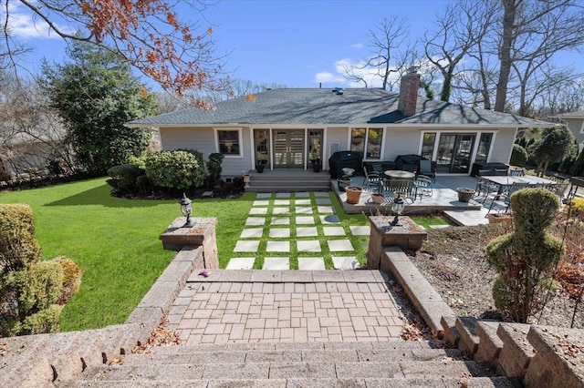 rear view of property with a lawn, french doors, roof with shingles, a chimney, and a patio area