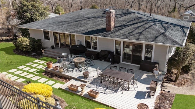 rear view of property with a fire pit, a wooden deck, roof with shingles, a chimney, and outdoor dining area