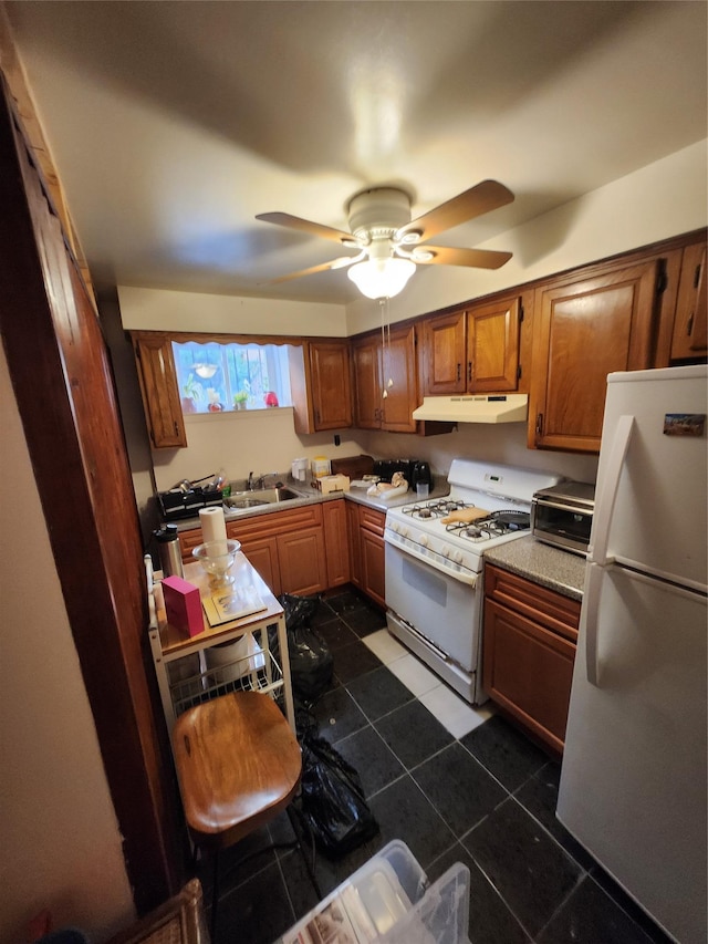 kitchen with white appliances, brown cabinetry, ceiling fan, under cabinet range hood, and dark tile patterned floors