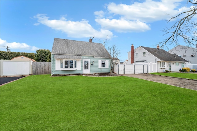 cape cod-style house with fence, roof with shingles, a gate, a chimney, and a front yard