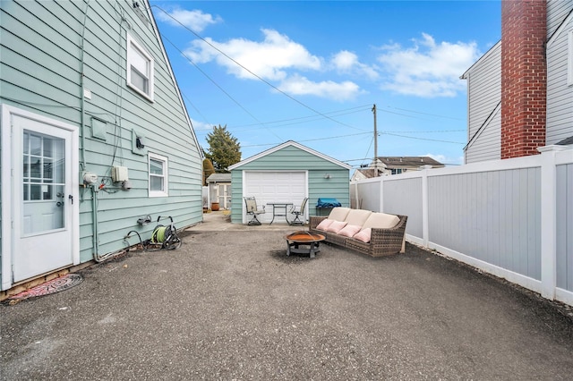 view of patio featuring driveway, an outdoor fire pit, a detached garage, fence, and an outdoor structure