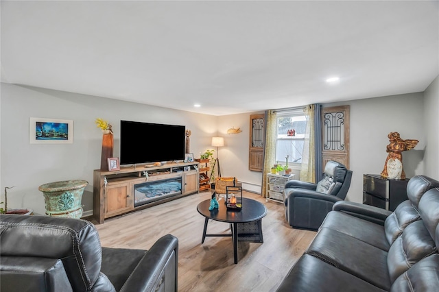 living area with a baseboard heating unit, baseboards, light wood-style flooring, and recessed lighting