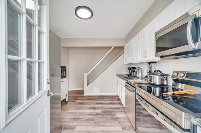 kitchen featuring light wood-style flooring, a sink, white cabinetry, appliances with stainless steel finishes, and decorative backsplash