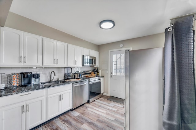 kitchen with tasteful backsplash, dark stone counters, stainless steel appliances, white cabinetry, and a sink