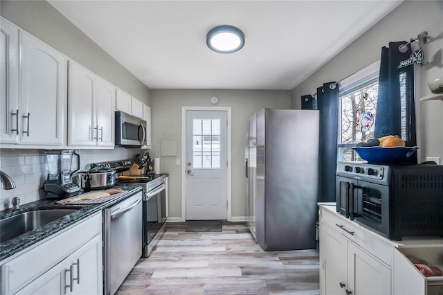 kitchen featuring stainless steel appliances, backsplash, light wood-style flooring, white cabinetry, and a sink