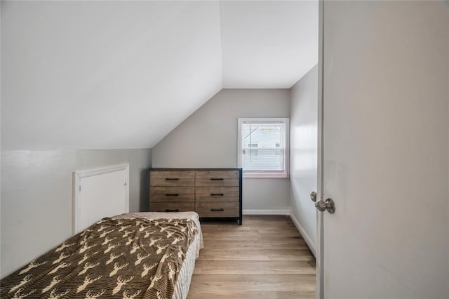 bedroom featuring lofted ceiling, baseboards, and light wood finished floors