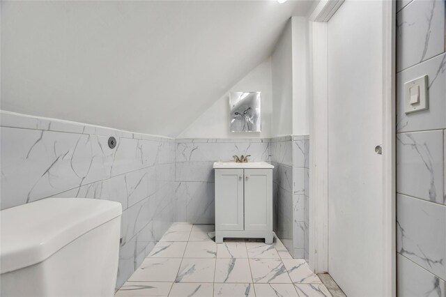 half bath with toilet, marble finish floor, vaulted ceiling, vanity, and tile walls