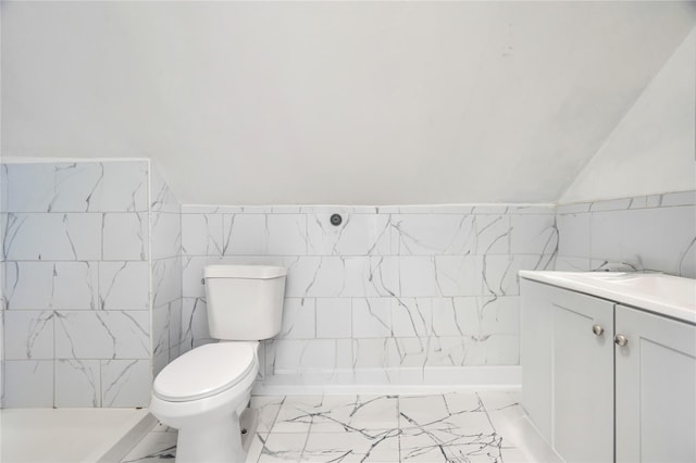 bathroom featuring marble finish floor, tile walls, toilet, vaulted ceiling, and vanity