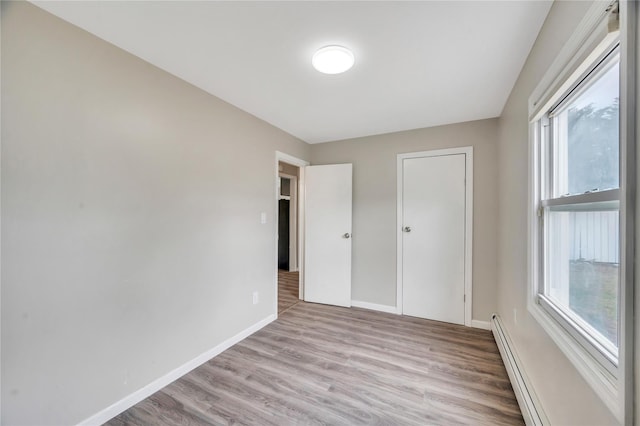 unfurnished bedroom with a baseboard heating unit, wood finished floors, and baseboards