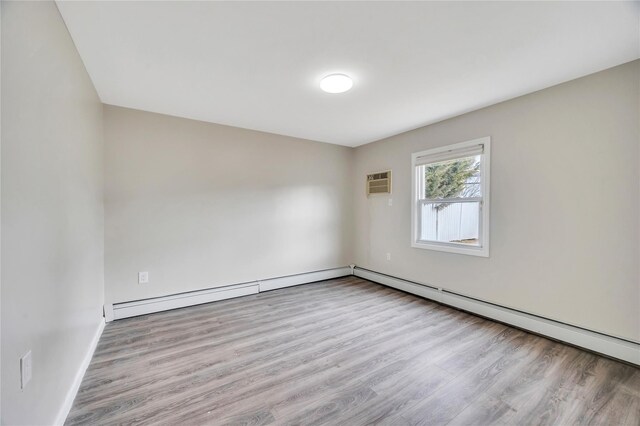 spare room featuring baseboards, a baseboard heating unit, wood finished floors, and a wall mounted air conditioner