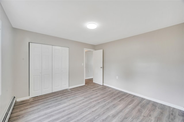 unfurnished bedroom featuring baseboards, a closet, a baseboard heating unit, and wood finished floors