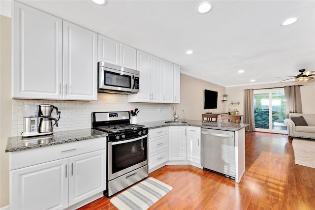 kitchen with stainless steel appliances, open floor plan, white cabinetry, a sink, and a peninsula