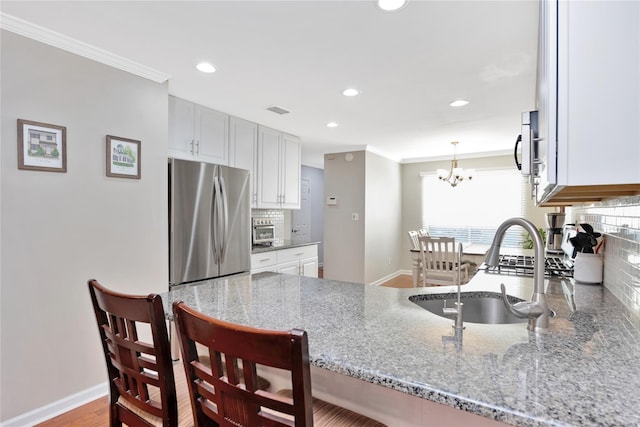 kitchen with light stone counters, freestanding refrigerator, a peninsula, crown molding, and a sink