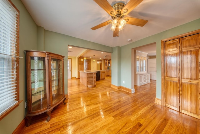 unfurnished living room featuring light wood-type flooring, a healthy amount of sunlight, baseboards, and a ceiling fan