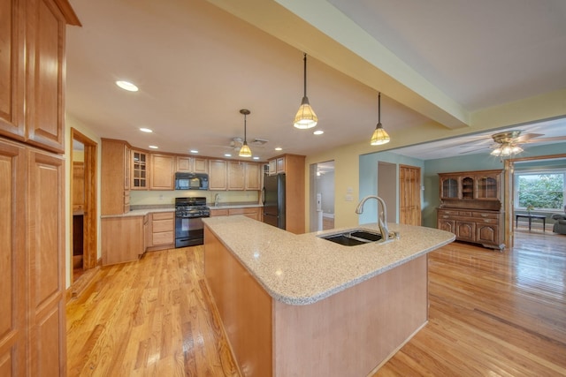 kitchen featuring light wood-style flooring, a ceiling fan, a kitchen island with sink, a sink, and black appliances